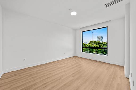 Empty room with wooden floor and a window showing a building and trees outside.