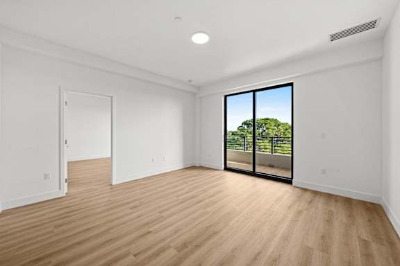 A room with a sliding glass door leading to a balcony with a view of trees.
