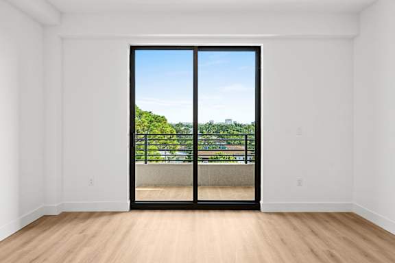 A room with a sliding door leading to a balcony with a view of a green landscape.
