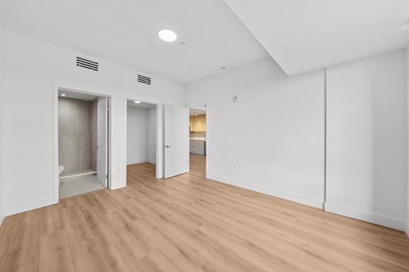 A room with white walls and wooden flooring with two open doors.