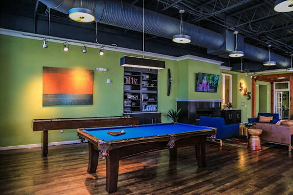 A pool table is in the middle of a room with a green wall and a TV mounted on the wall.