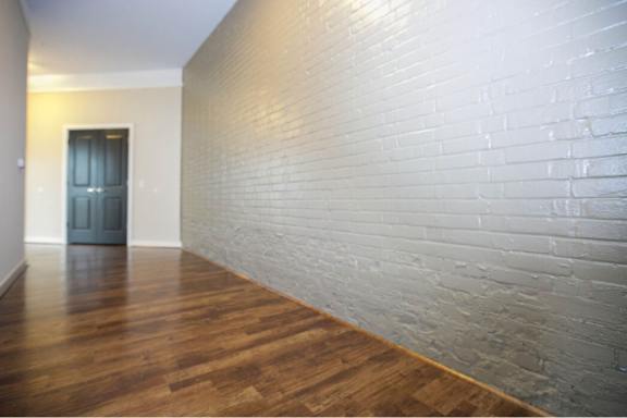 A long hallway with a wooden floor and a white brick wall.
