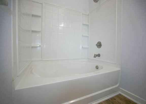 A white bathtub in a bathroom with a white tile wall.