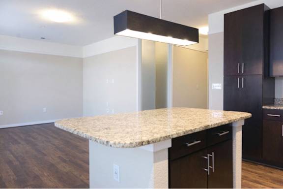 A kitchen with a granite countertop and dark brown cabinets.