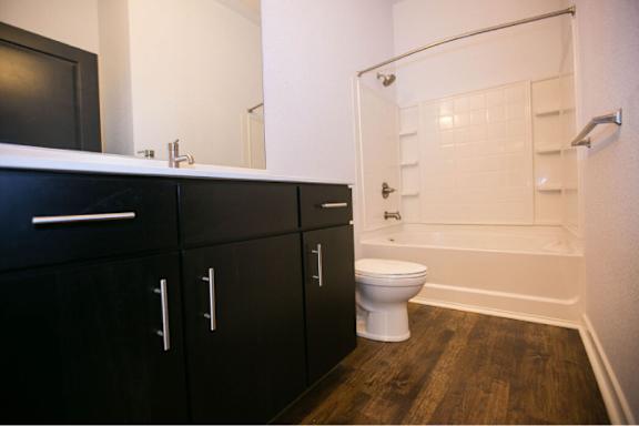 A white toilet sits in a bathroom with black cabinets and a white shower.