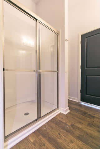 A bathroom with a glass door shower enclosure and a black door.