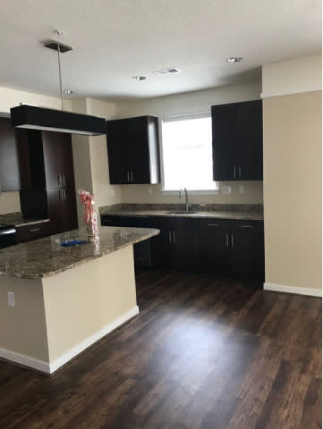 A kitchen with dark wood floors and a granite counter.