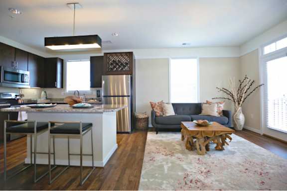 A kitchen with a bar and stools is adjacent to a living room with a couch and a coffee table.
