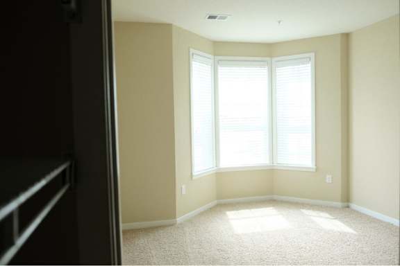 A room with a carpeted floor and a window with blinds.