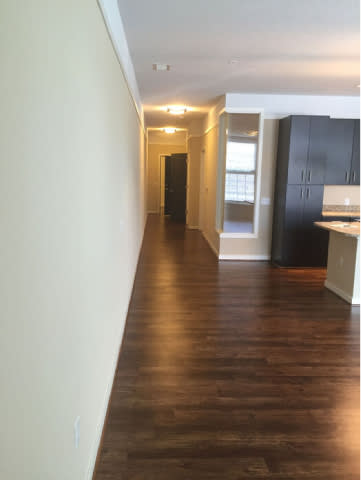 A long hallway with a black trash can and a kitchen area in the distance.