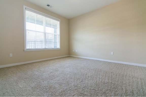 A room with a carpeted floor and a window with blinds.
