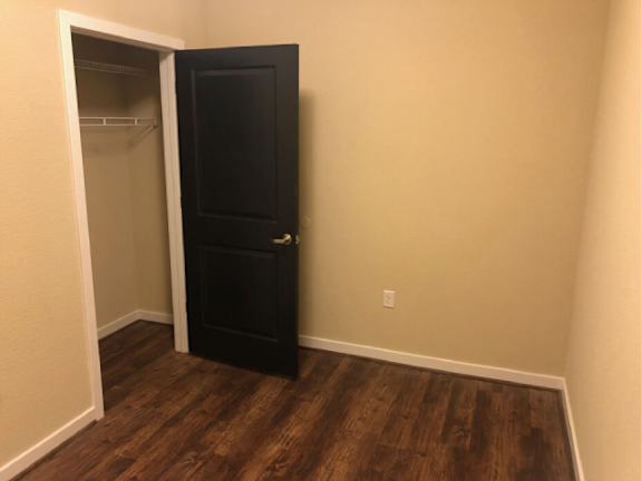 A black door is open to a room with wood flooring.