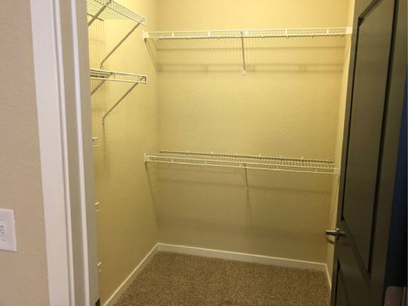 Empty walk-in closet with white shelves and carpeted floor.
