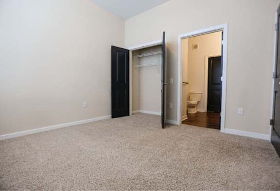 A room with a carpeted floor and a closet with a door open to a bathroom.