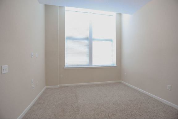 A room with a carpeted floor and a window with blinds.
