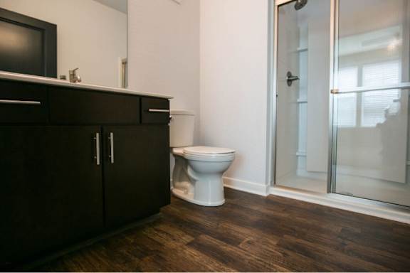 A white toilet sits in a bathroom with a wooden floor and a glass shower door.