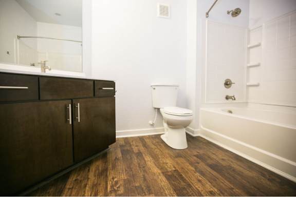 A white toilet sits in a bathroom with wooden floors and white walls.
