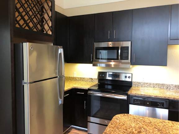 A kitchen with black cabinets and a stainless steel refrigerator.