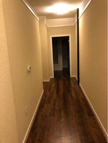 A long hallway with wood floors and a door at the end.