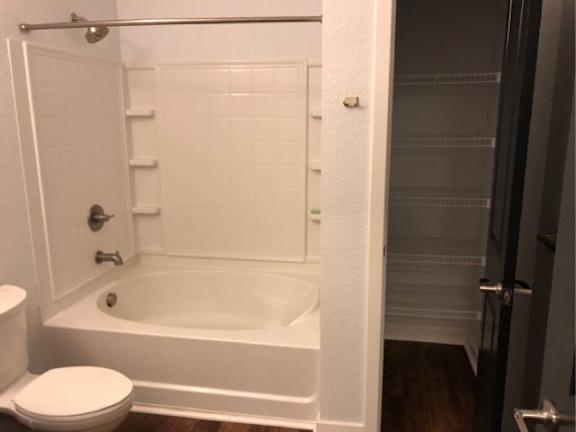 A white bathroom with a toilet, tub, and shelves.