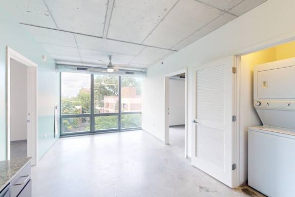 A white room with a washing machine and a window with a view of trees.