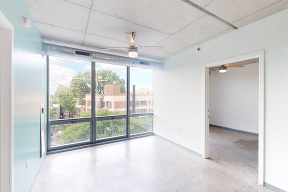 A room with a ceiling fan and a large window overlooking a cityscape.