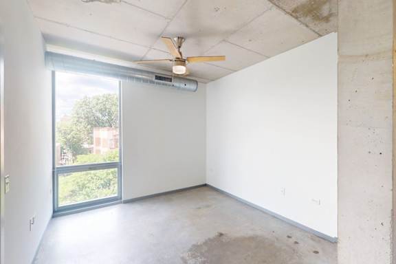 A room with a ceiling fan and a window overlooking a tree.