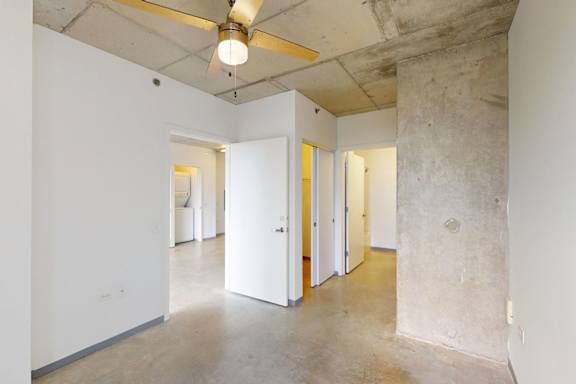 A room with a concrete floor and walls with a ceiling fan.