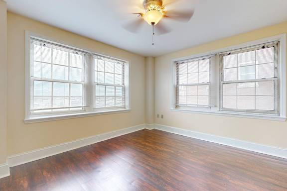 A room with a ceiling fan and two windows.