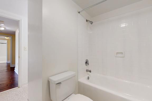 A white toilet is in a bathroom with a white tub.