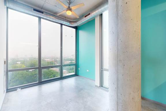 A room with a ceiling fan and a view of the outside through the windows.