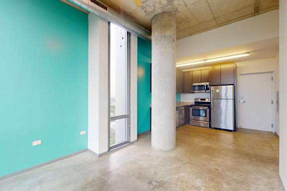 A kitchen with a refrigerator, microwave, and oven is visible through a glass door.