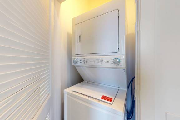 A white dryer is sitting in a small, white-walled laundry room.