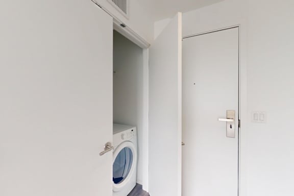 A white washing machine is in a small alcove in a white wall.