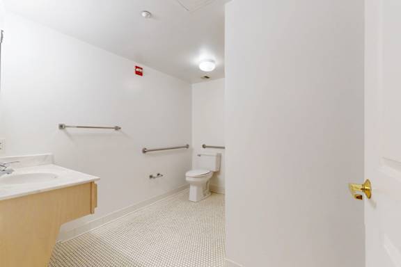 A white bathroom with a toilet, sink, and grab bar.