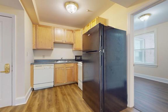 A kitchen with a black refrigerator, wooden cabinets, and a white dishwasher.