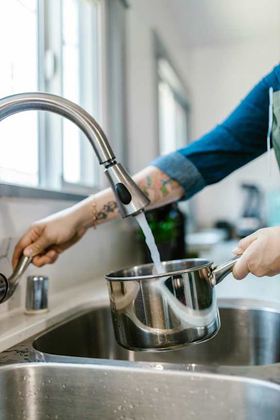 A person is pouring water from a tap into a pot.