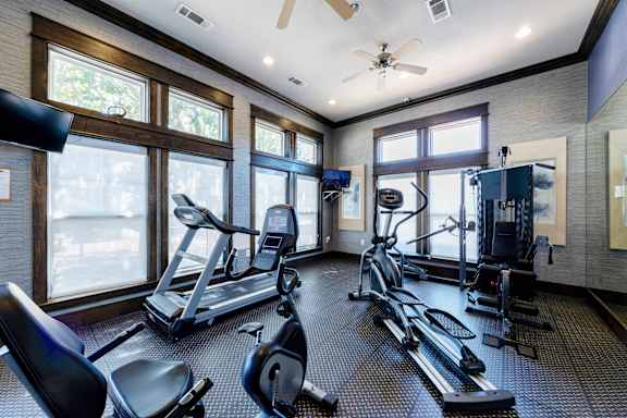 A spacious gym with treadmills, elliptical machines, and a ceiling fan.