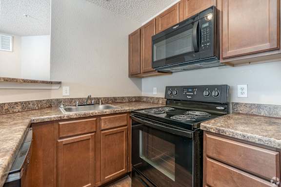 A black microwave oven is mounted above a black stove in a kitchen.