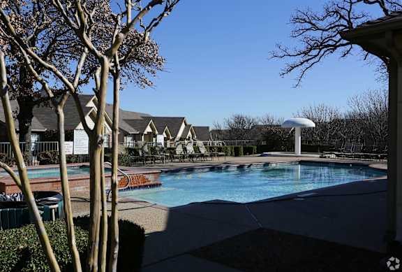 A pool surrounded by trees and a building in the background.