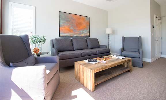 A living room with a grey couch, a wooden coffee table, and a painting on the wall.