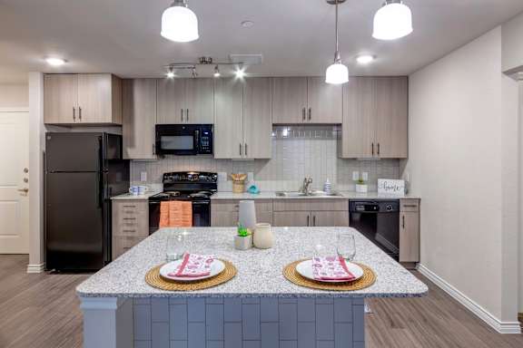 A kitchen with a black refrigerator and a granite countertop.