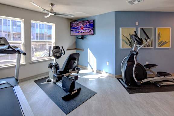 A room with a treadmill, a stationary bike, and a television playing a basketball game.