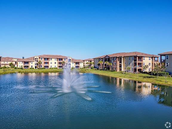 A fountain in the middle of a lake in front of apartment buildings.