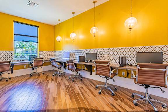 A room with yellow walls and wooden floors has a long table with chairs and computers on it.