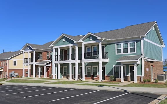 A large building with a green and white facade has a parking lot in front.