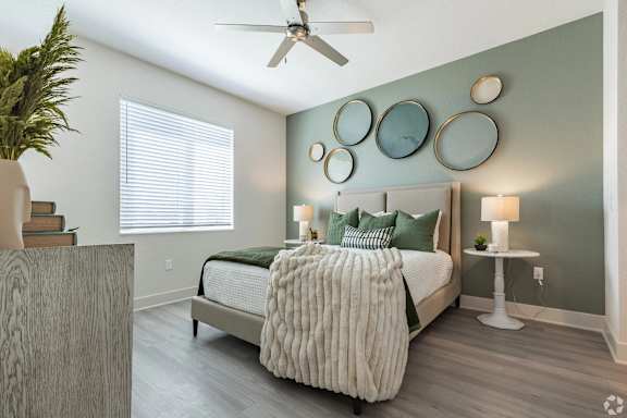 A bedroom with a bed, a potted plant, and a ceiling fan.