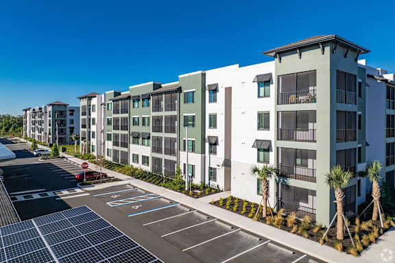 A row of modern apartment buildings with a parking lot in front.