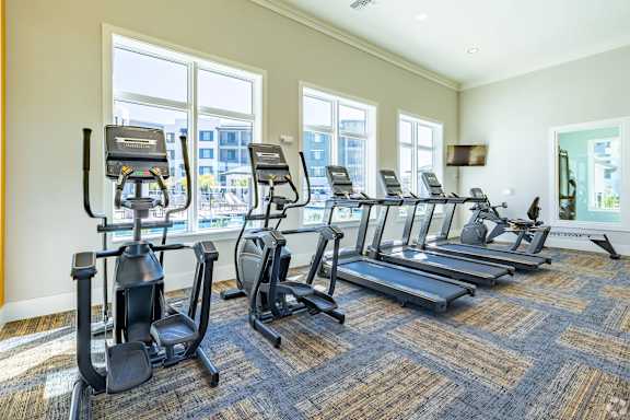 A gym with treadmills, elliptical machines, and a weight bench.