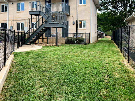 A black metal fence surrounds a green lawn in front of a building.